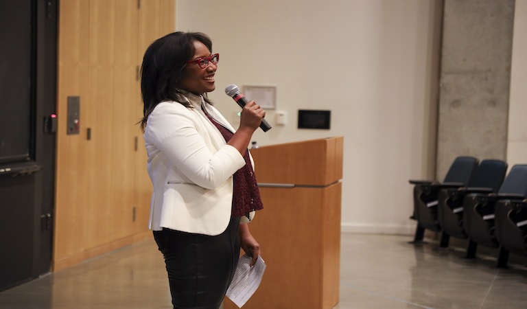 Talithia Williams holds a microphone while addressing a lecture hall.